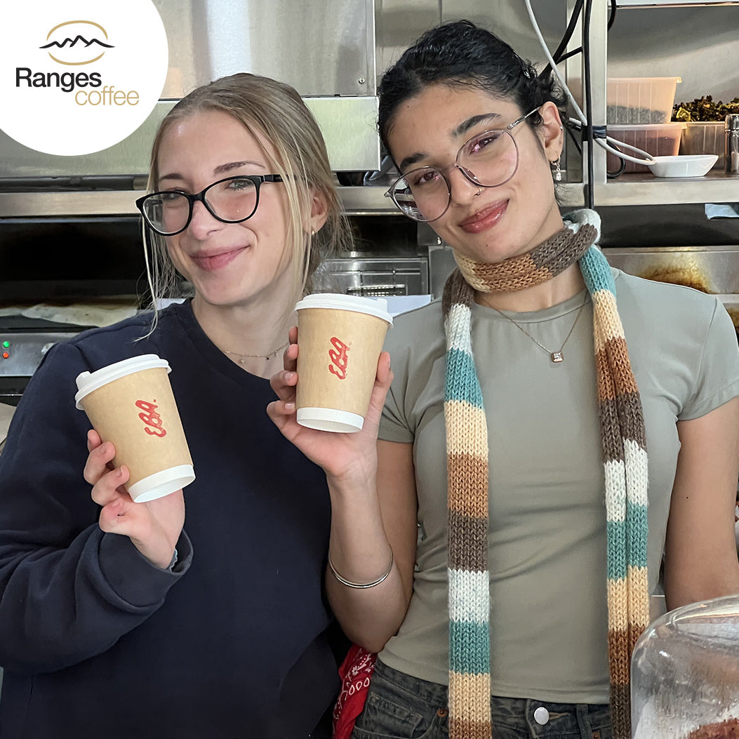 Two people holding coffee cups with Ranges Coffee logo in a kitchen setting.